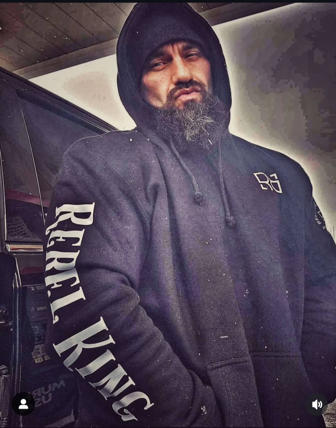 Man wearing a hoodie with 'Rebel King' text, standing next to a car.