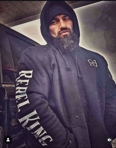 Man wearing a hoodie with 'Rebel King' text, standing next to a car.