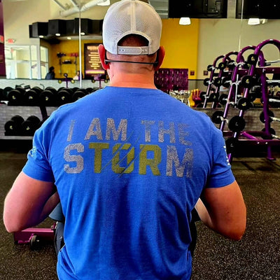 Person wearing a blue t-shirt with 'I AM THE STORM' text in a gym setting