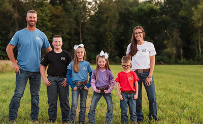 Family of six standing in a grassy field with trees in the background