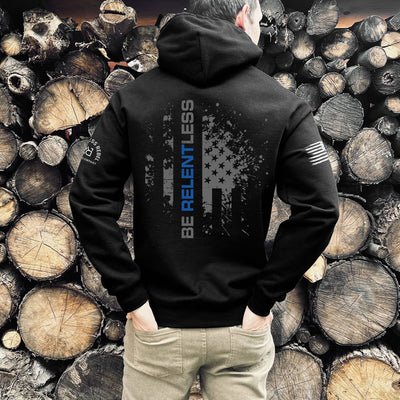 Person wearing a black hoodie with text and logos, standing against a background of stacked wooden logs.
