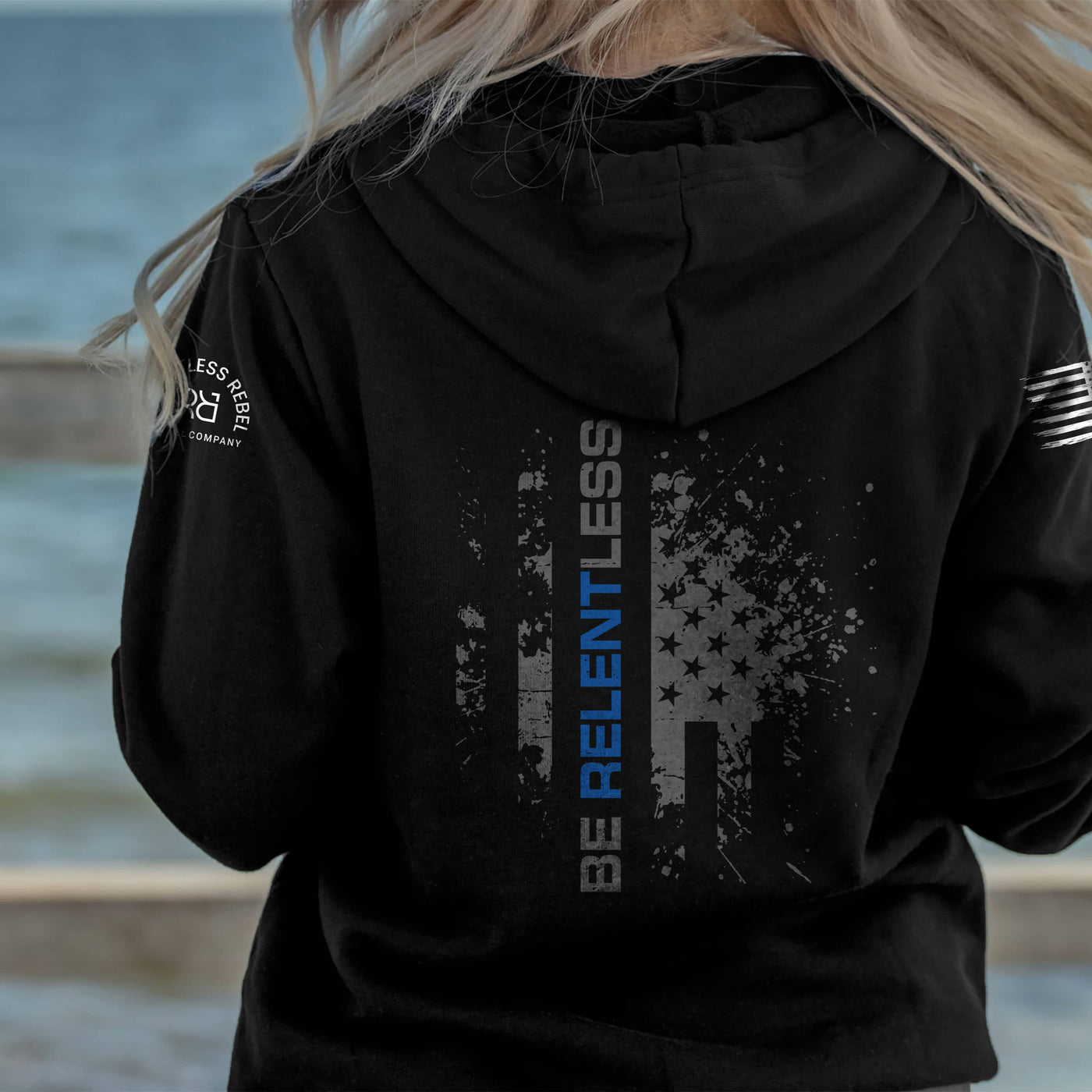 Person wearing a black hoodie with a graphic design by the water