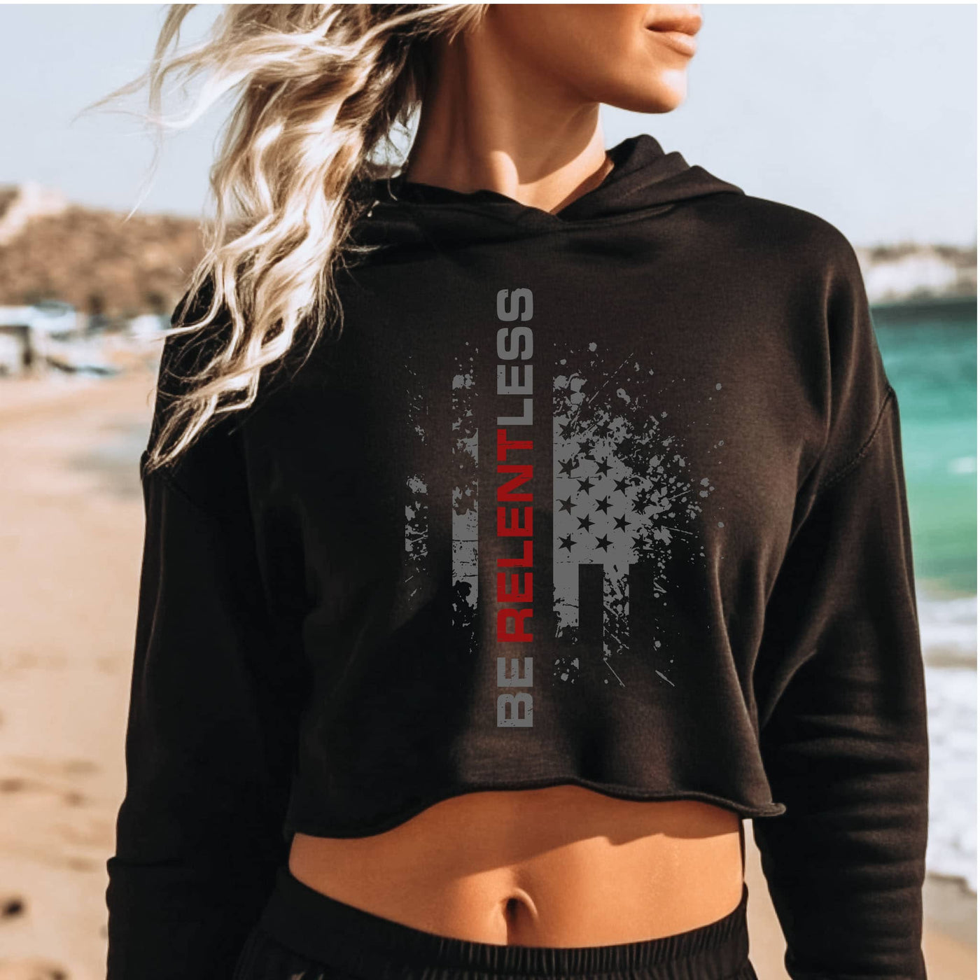 Person wearing a black hoodie with 'Be Relentless' text on a beach