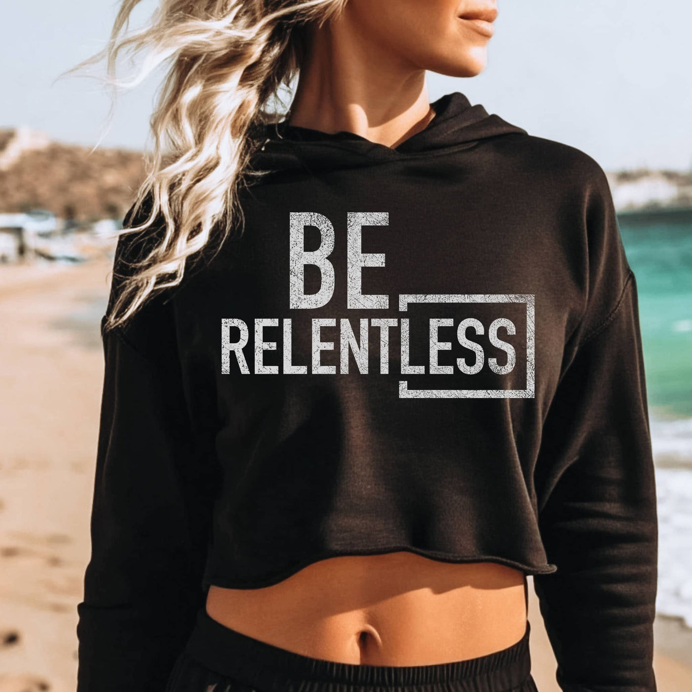 Person wearing a black hoodie with 'BE RELENTLESS' text on a beach