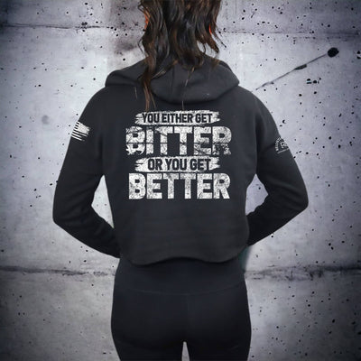 Person wearing a black hoodie with motivational text on the back against a gray concrete wall.