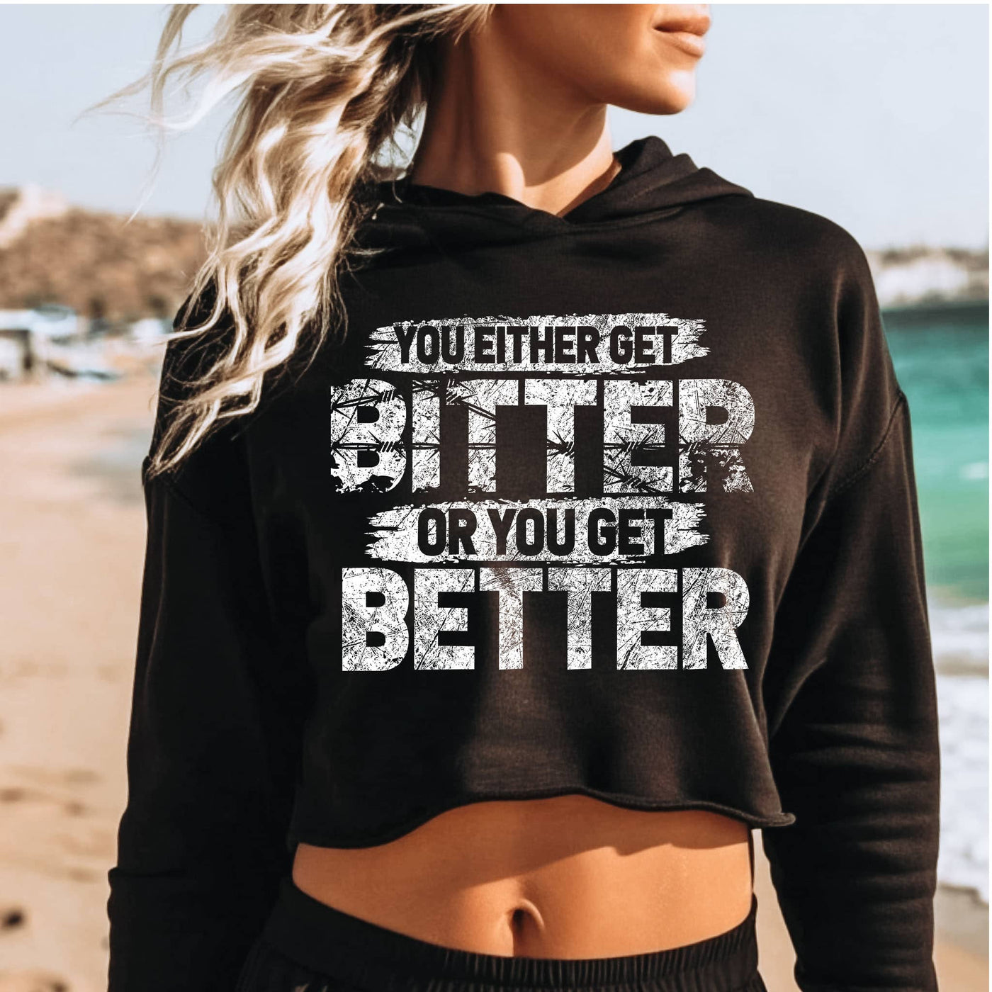 Person wearing a black hoodie with motivational text on a beach