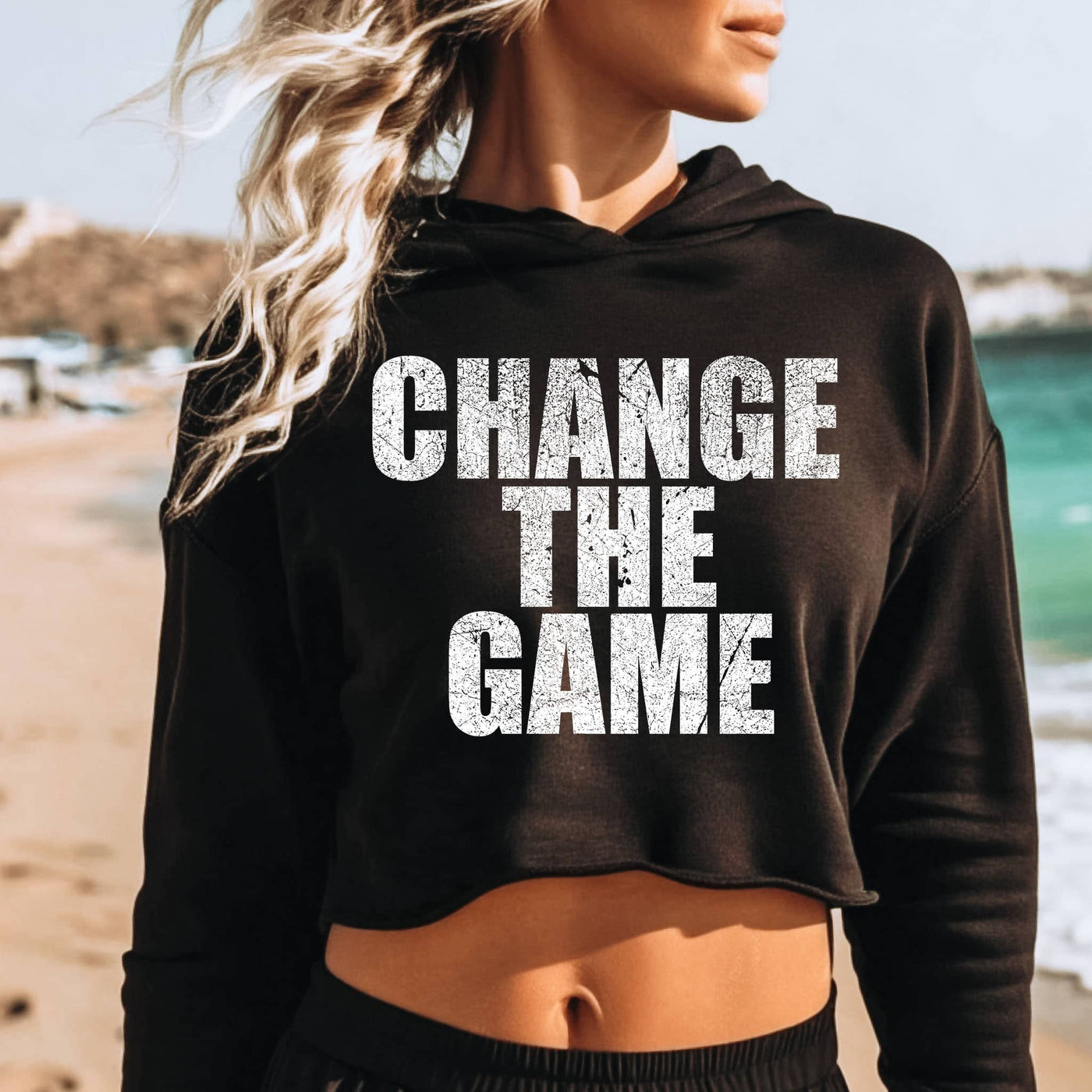 Person wearing a black hoodie with 'CHANGE THE GAME' text on a beach.
