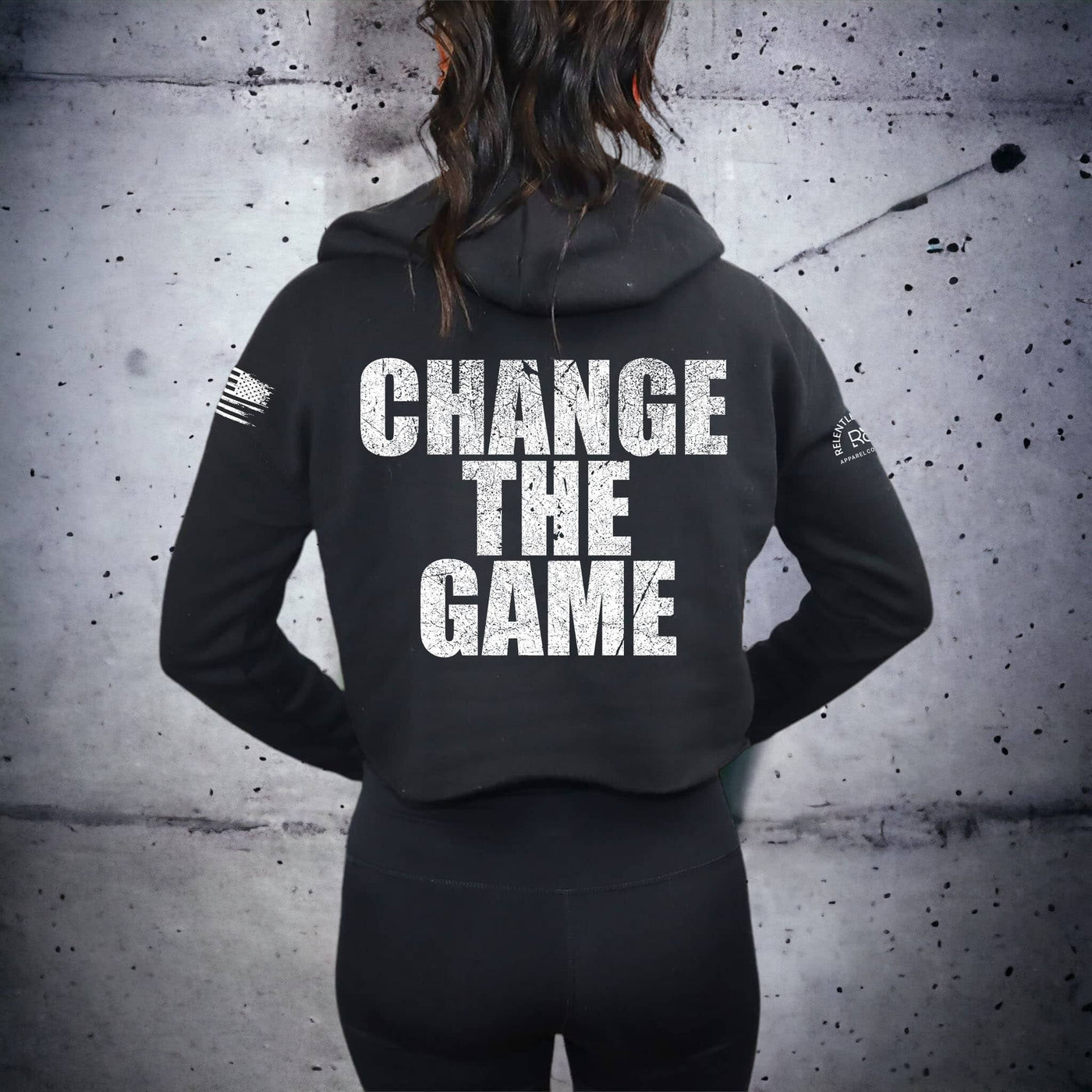 Person wearing a black hoodie with 'CHANGE THE GAME' text on the back against a textured wall.