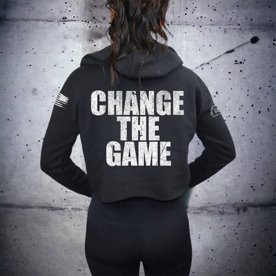 Person wearing a black hoodie with 'CHANGE THE GAME' text on the back against a textured wall.