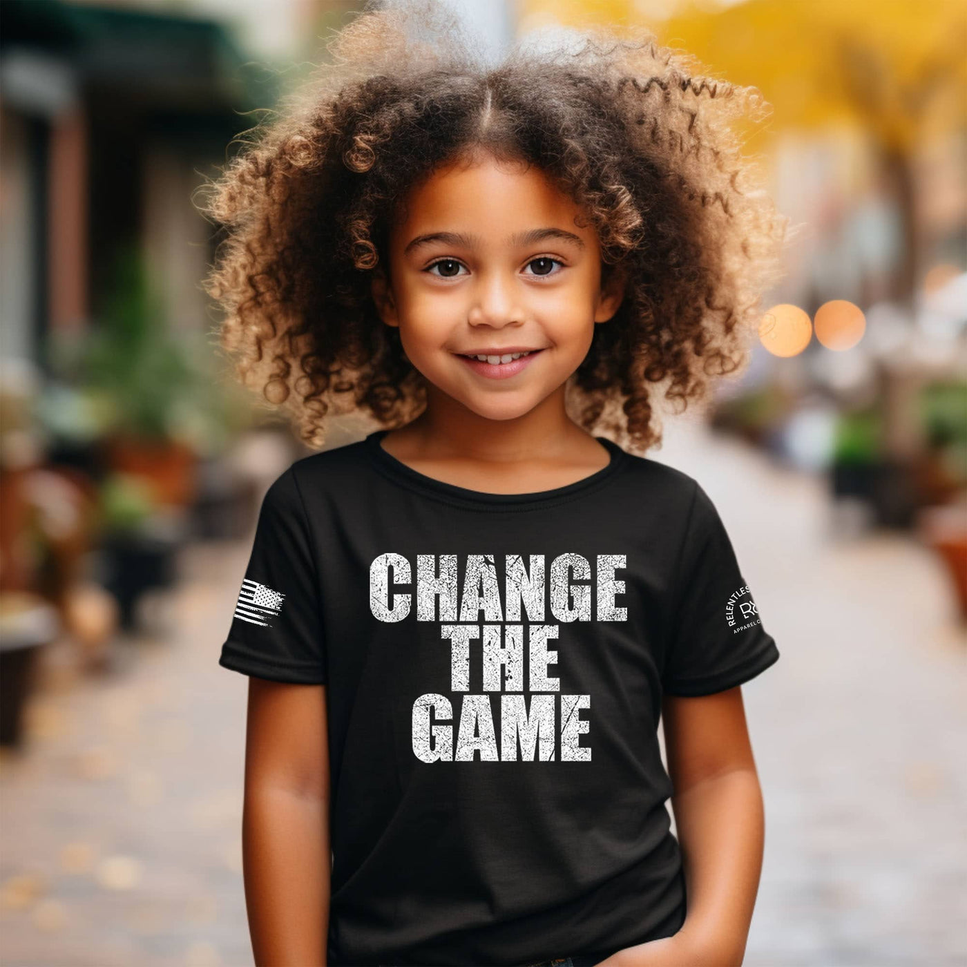 Child wearing a black t-shirt with 'CHANGE THE GAME' text in an outdoor setting