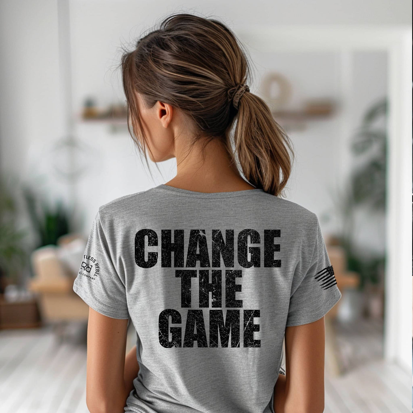 Person wearing a gray t-shirt with 'CHANGE THE GAME' text on the back in a blurred indoor setting.