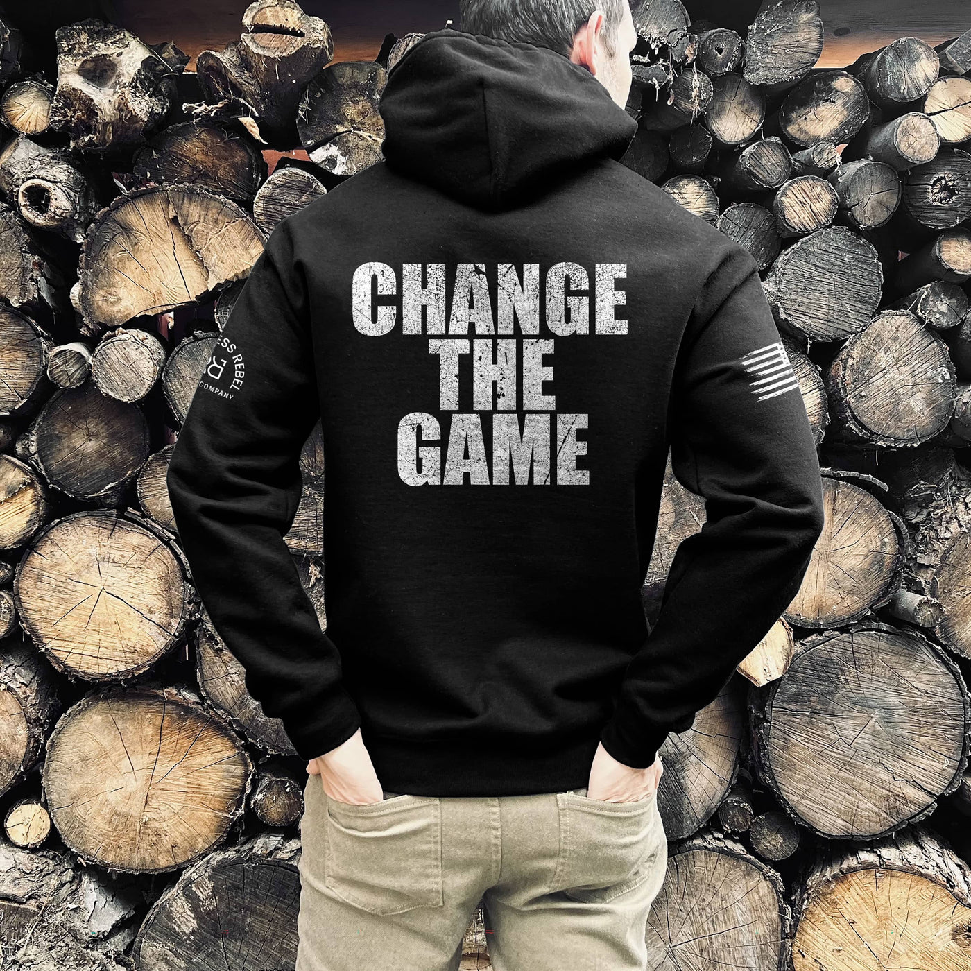 Person wearing a black hoodie with 'CHANGE THE GAME' text, standing against a background of stacked wooden logs.