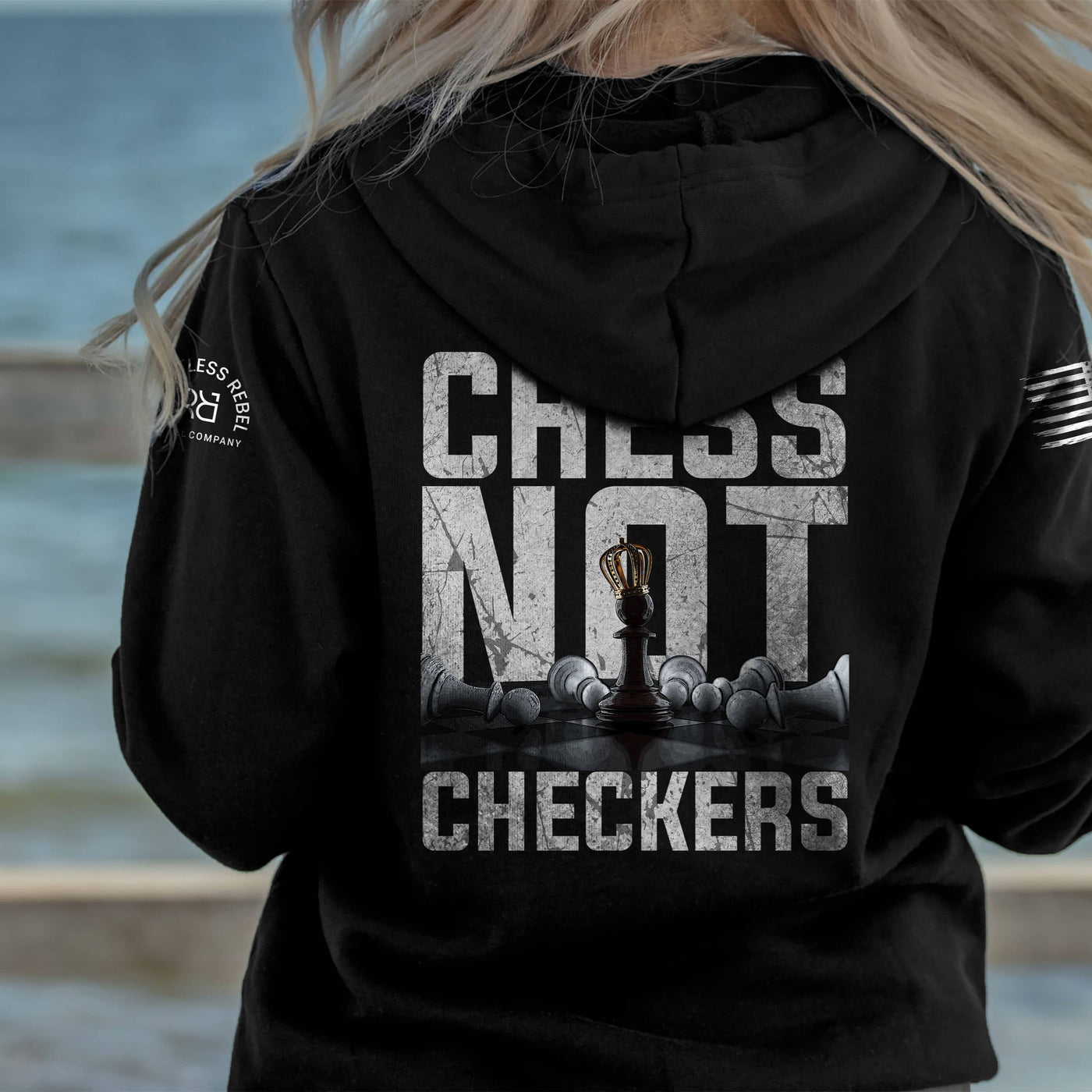Person wearing a black hoodie with 'Chess Not Checkers' design by the water