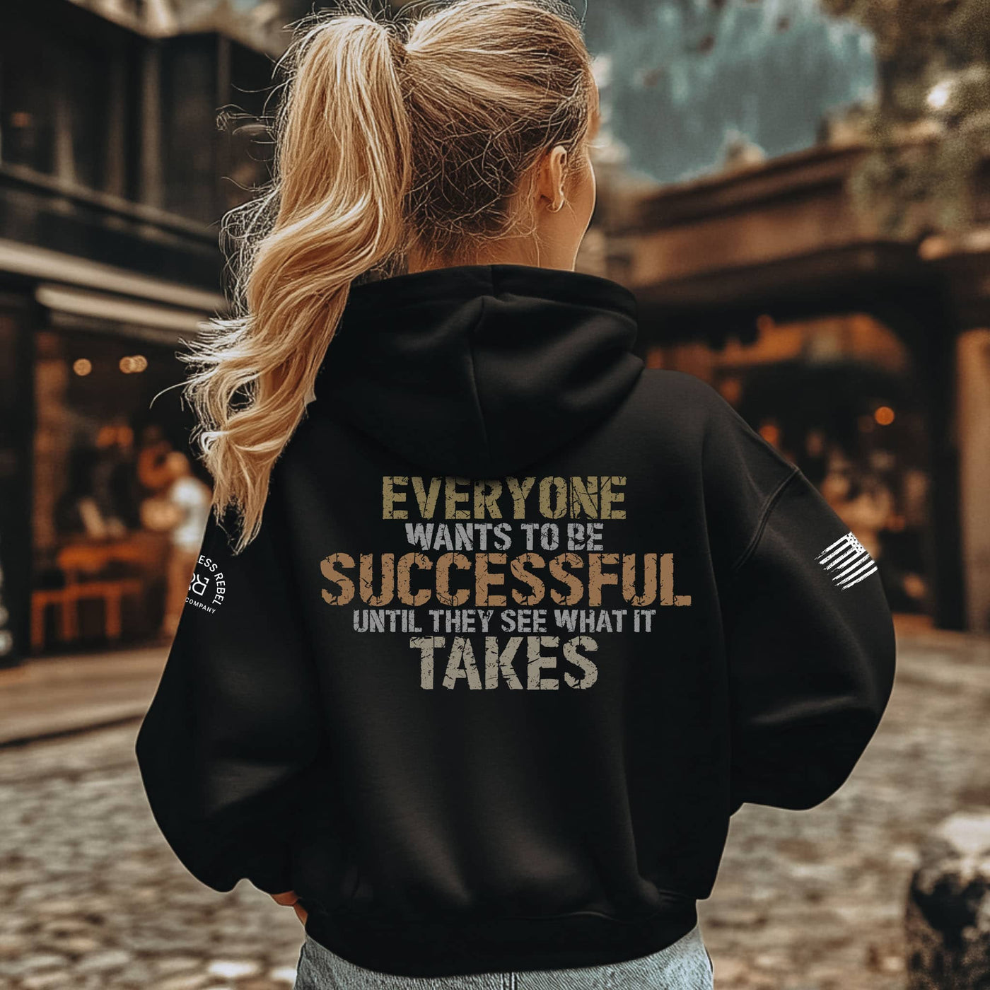 Person wearing a black hoodie with motivational text on the back, standing outdoors.