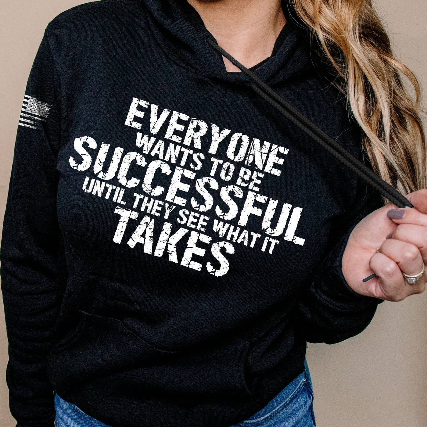 Person wearing a black hoodie with motivational quote on a beige background