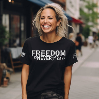 Woman wearing a black t-shirt with 'Freedom is Never Free' text on a city street.