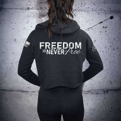 Person wearing a black hoodie with 'Freedom is Never Free' text on the back against a textured wall.