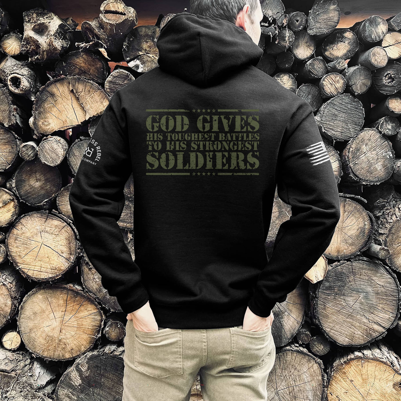 Person wearing a black hoodie with text in front of stacked wooden logs
