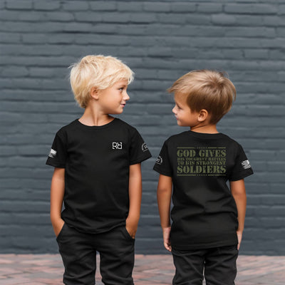 Two children wearing black t-shirts with text and logos against a brick wall.