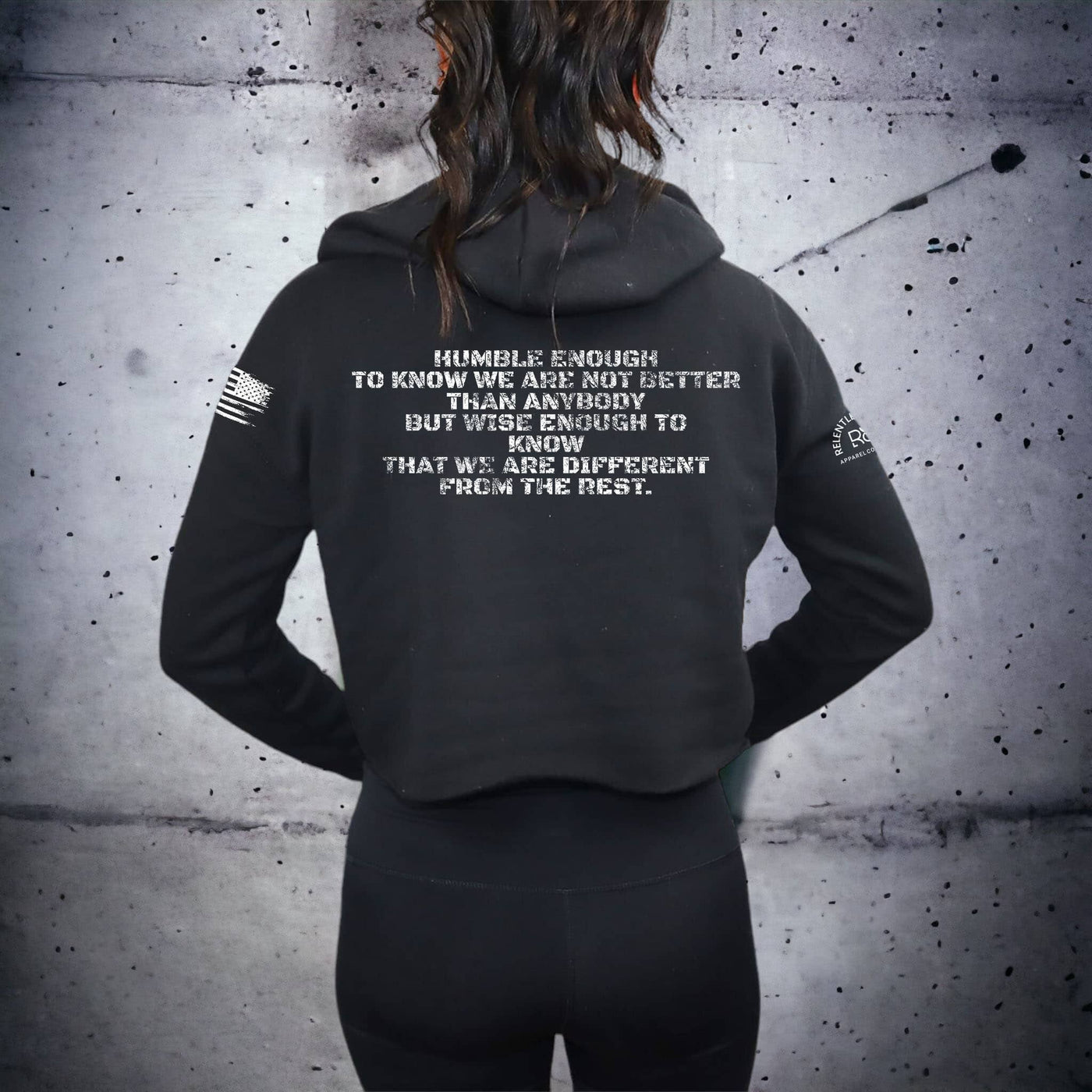 Person wearing a black hoodie with text on the back against a gray concrete wall.
