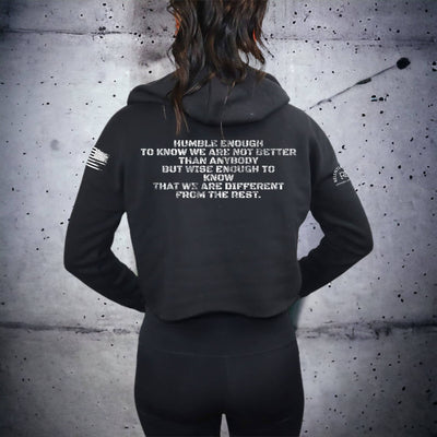 Person wearing a black hoodie with text on the back against a gray concrete wall.