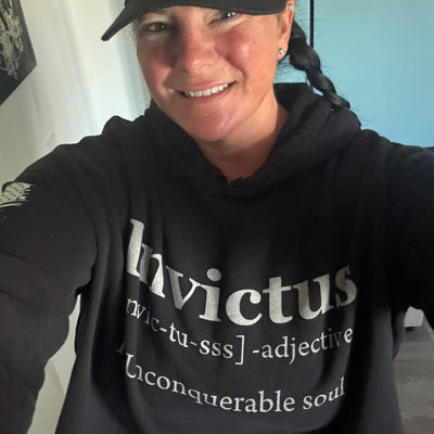 Person wearing a black hoodie with 'Invictus' text, smiling indoors.