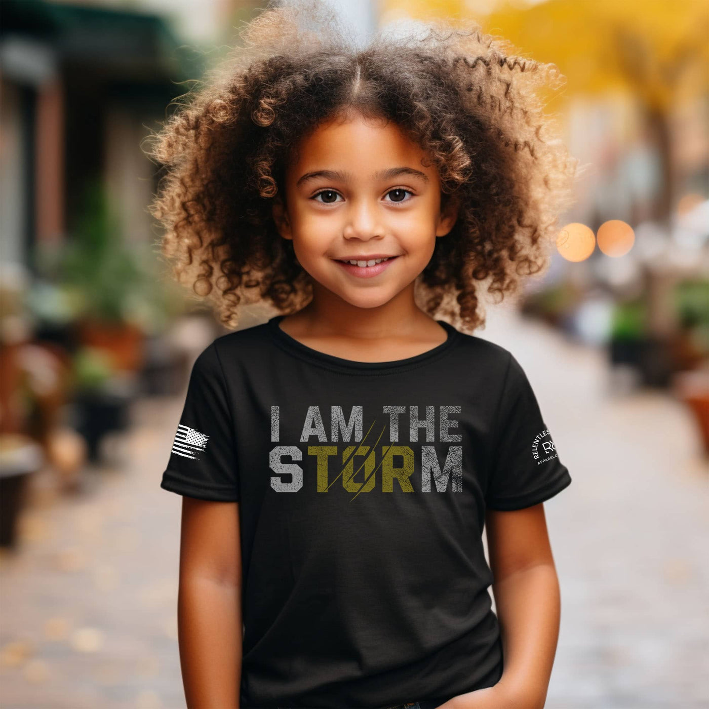 Child wearing a black t-shirt with 'I AM THE STORM' text in an outdoor setting