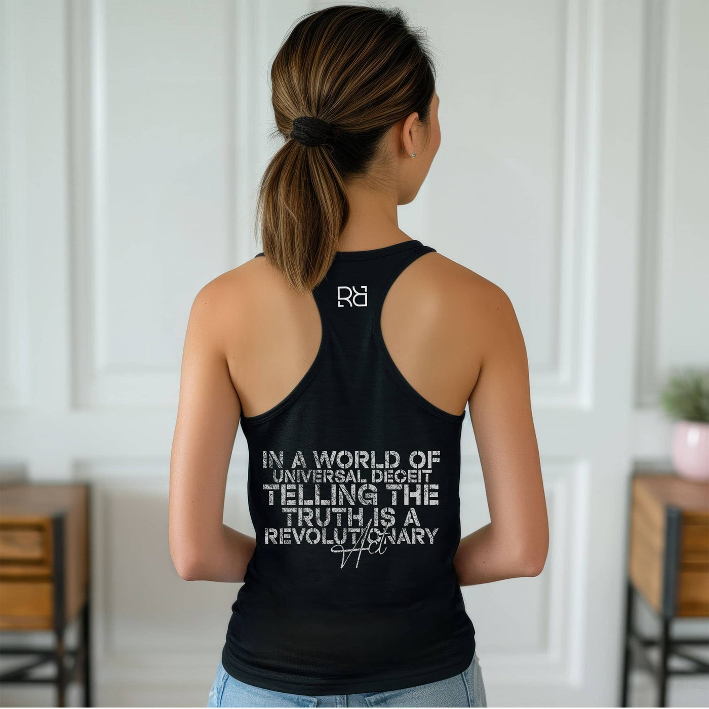 Person wearing a black tank top with text and a logo, standing in a room with wooden furniture.
