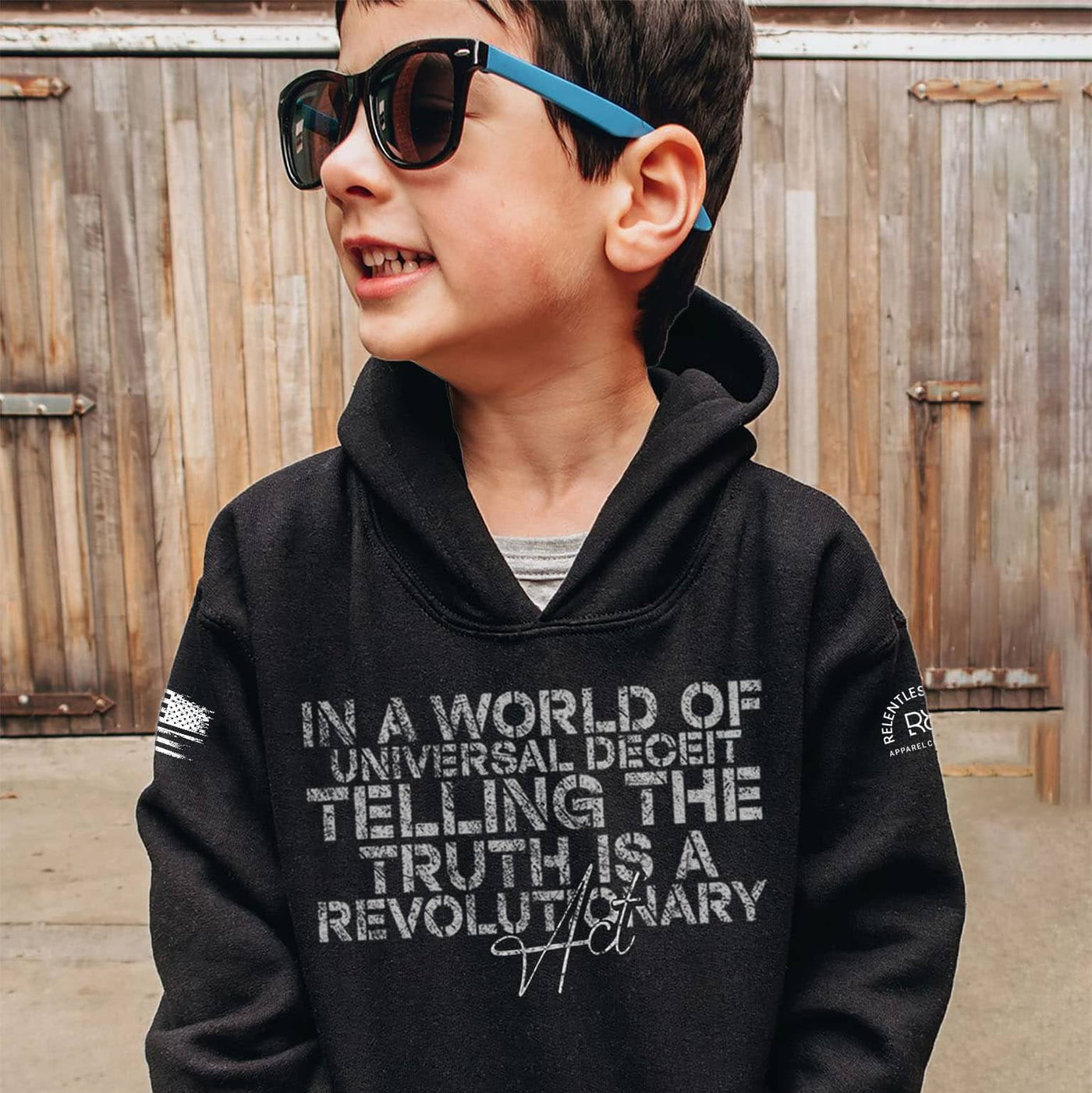 Child wearing a black hoodie with text in front of a wooden fence.