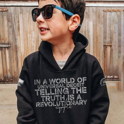 Child wearing a black hoodie with text in front of a wooden fence.
