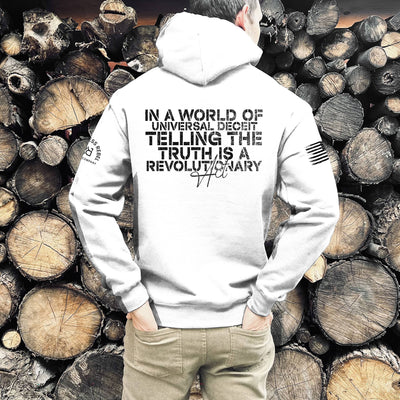 Person wearing a white hoodie with text in front of stacked logs