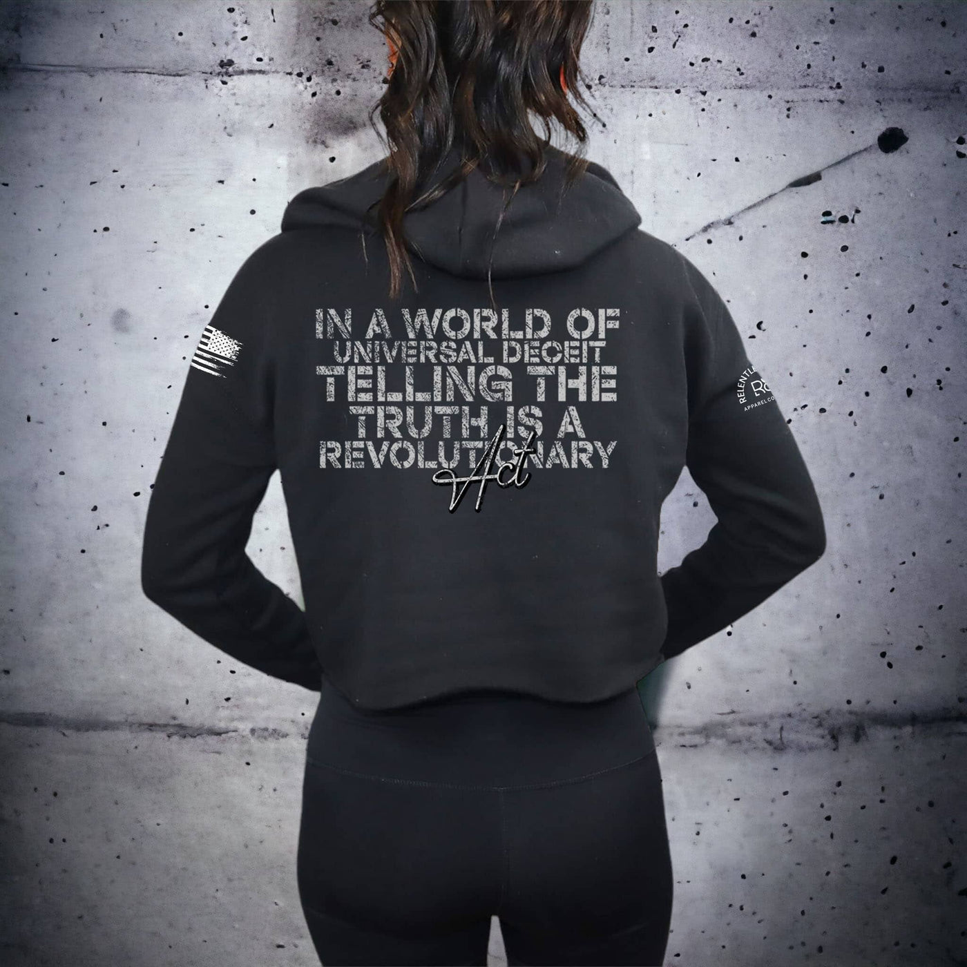 Person wearing a black hoodie with text on the back against a textured wall.