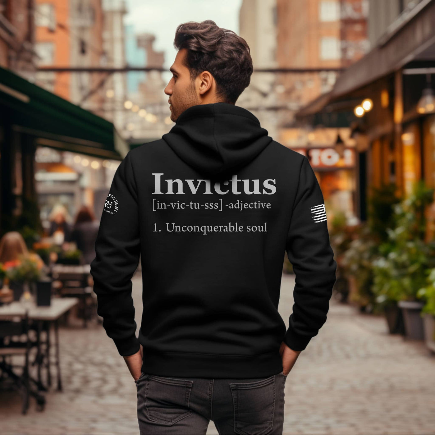 Man wearing a black hoodie with 'Invictus' text on the back in an urban setting.