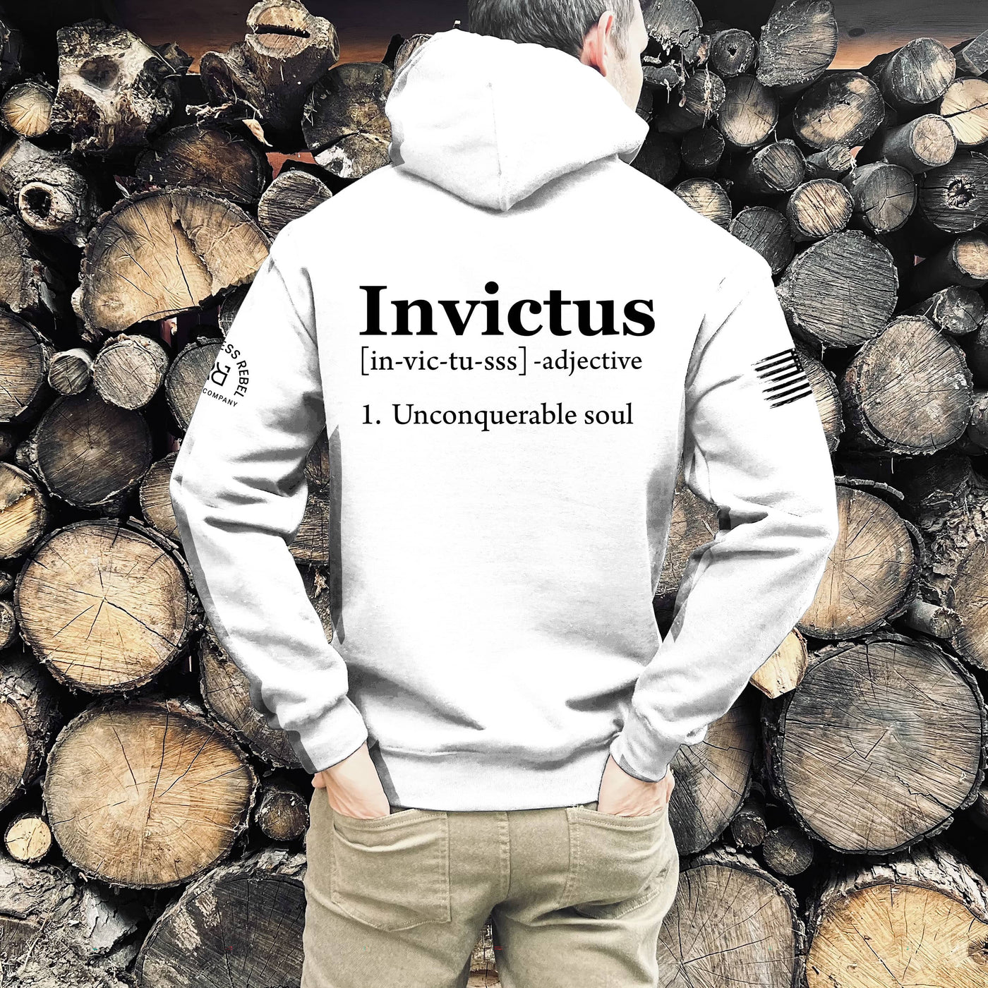 Person wearing a white hoodie with 'Invictus' text in front of stacked logs