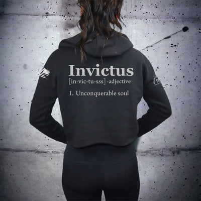 Person wearing a black hoodie with 'Invictus' text on the back against a textured wall.