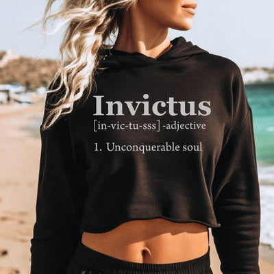 Person wearing a black hoodie with 'Invictus' text on a beach