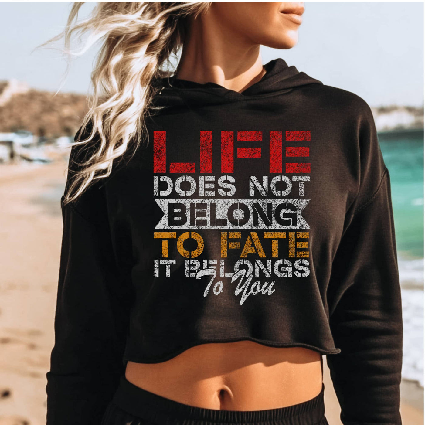 Person wearing a black hoodie with motivational quote on a beach
