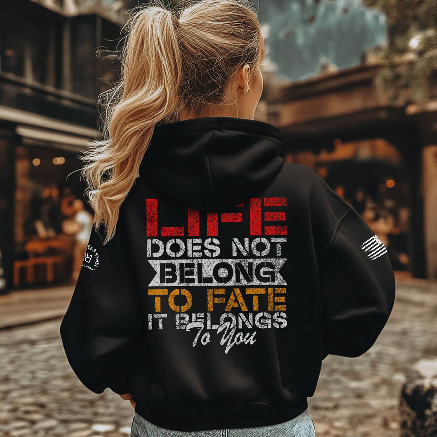 Person wearing a black hoodie with a motivational quote on the back, standing outdoors.