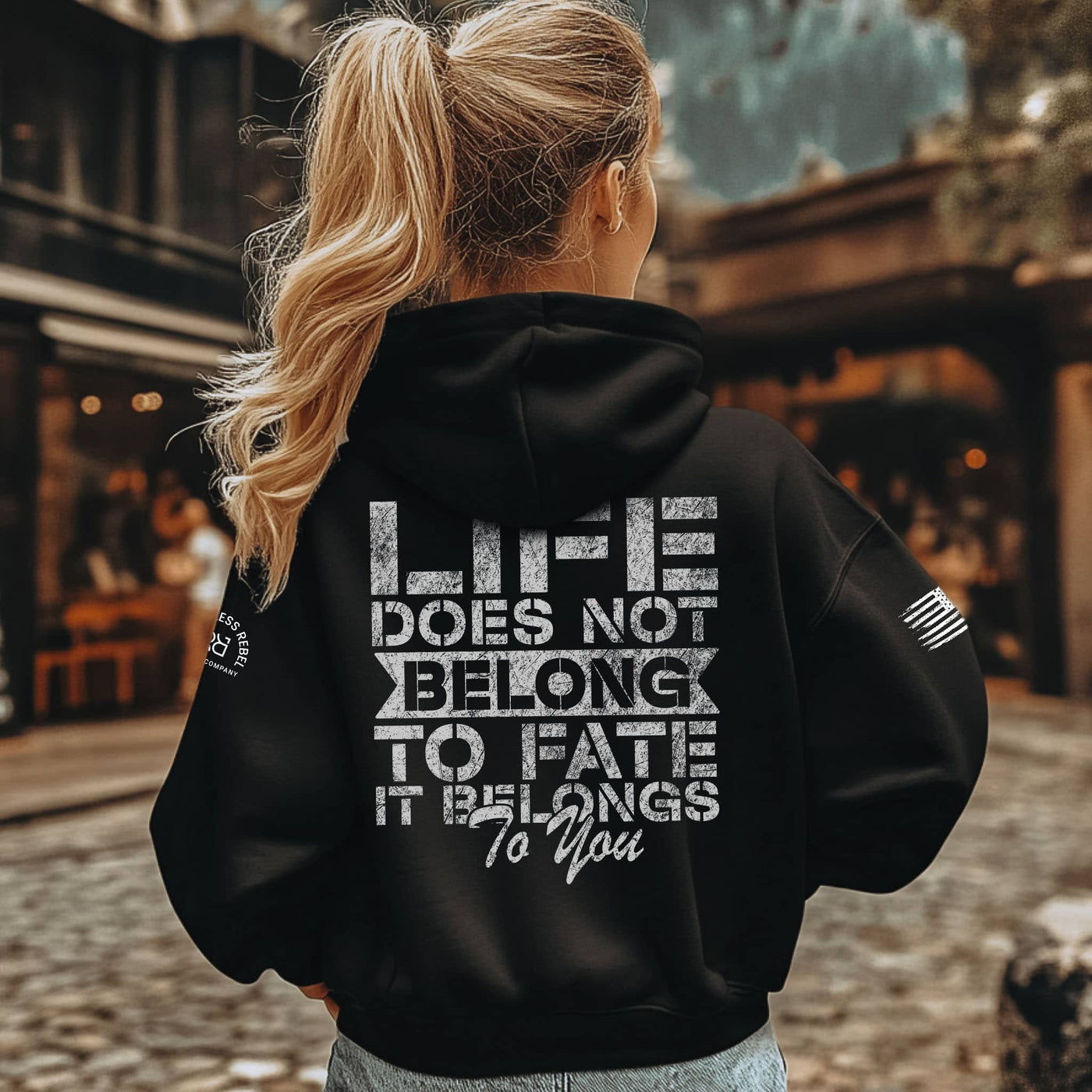Person wearing a black hoodie with a motivational quote on the back, standing outdoors.