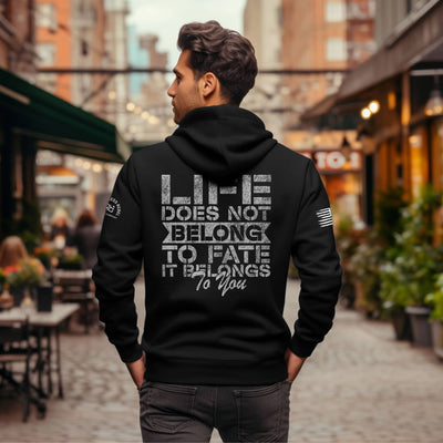 Man wearing a black hoodie with a motivational quote on the back in an urban setting.
