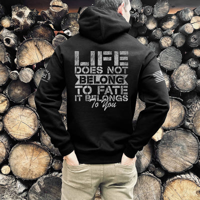 Person wearing a black hoodie with a motivational quote on the back, standing against a background of stacked wooden logs.