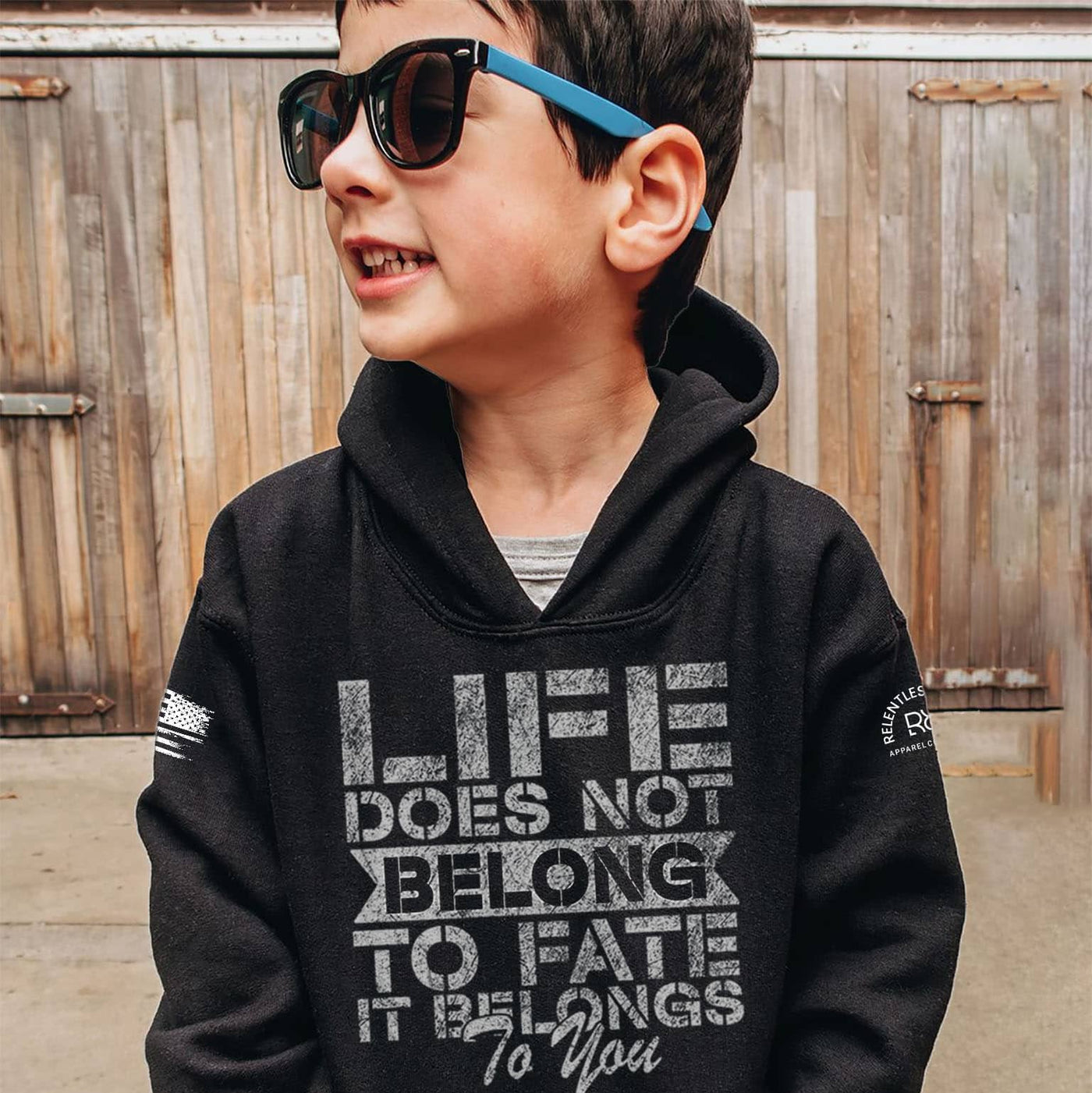 Child wearing a black hoodie with a motivational quote, standing in front of a wooden fence.