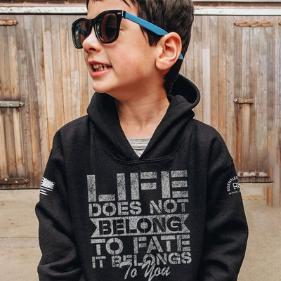 Child wearing a black hoodie with a motivational quote, standing in front of a wooden fence.
