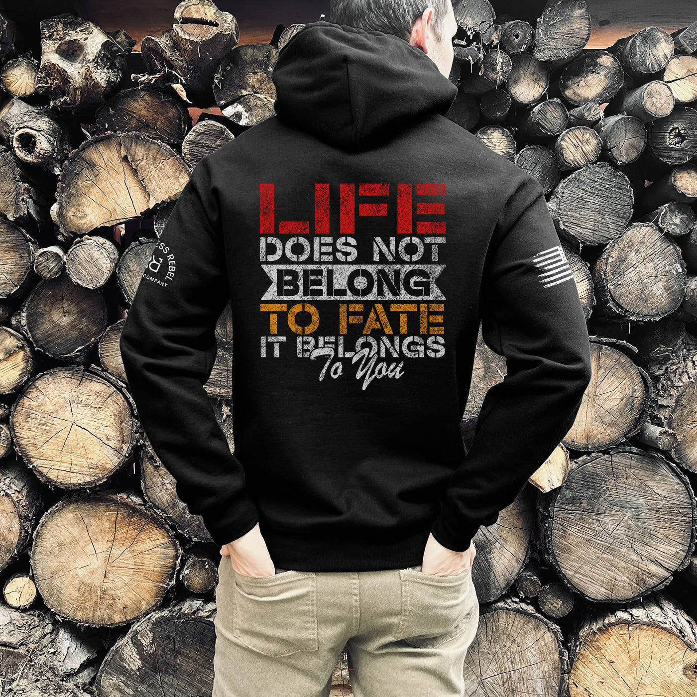 Person wearing a black hoodie with a motivational quote against a background of stacked wooden logs.