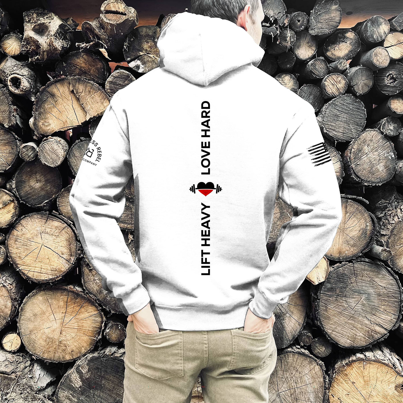 Person wearing a white hoodie with text and logos, standing against a background of stacked wooden logs.