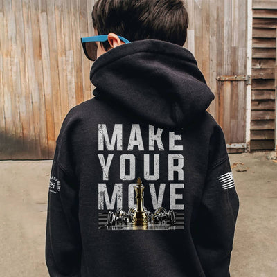 Person wearing a black hoodie with 'Make Your Move' text and chess piece design on the back, standing in front of wooden panels.