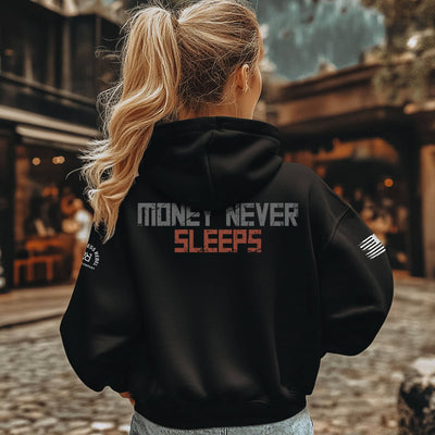 Person wearing a black hoodie with 'Money Never Sleeps' text on the back, standing outdoors.