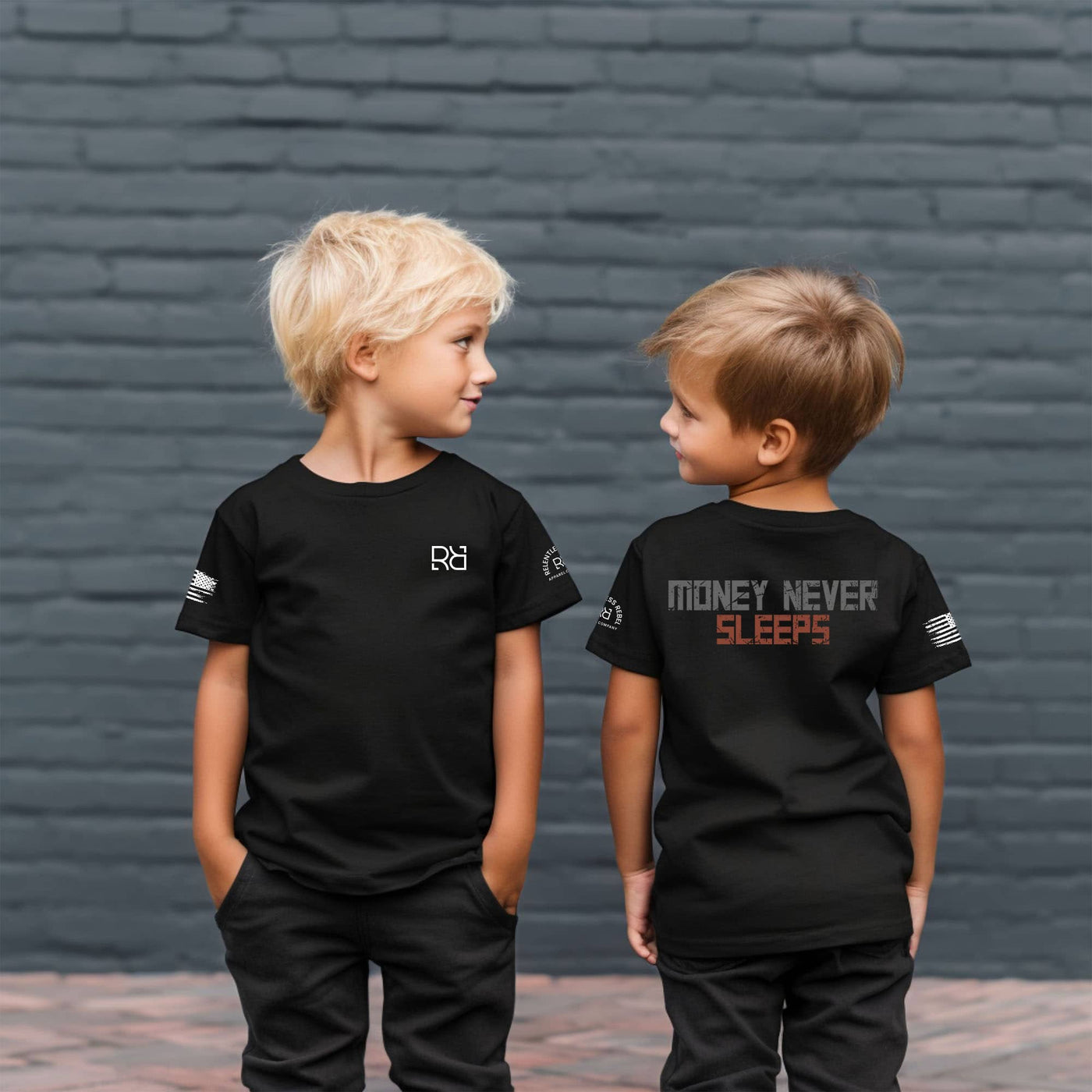 Two children wearing black t-shirts with text against a brick wall.