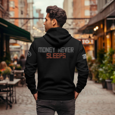 Man wearing a black hoodie with 'Money Never Sleeps' text on the back in an urban setting.