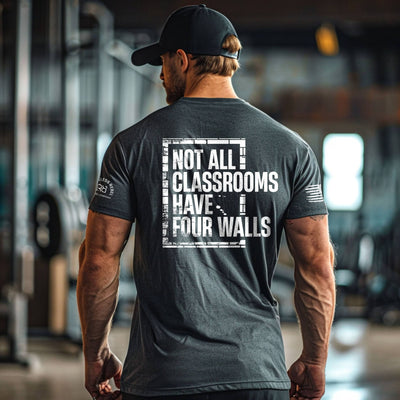 Man wearing a t-shirt with 'Not All Classrooms Have Four Walls' text in an indoor setting.